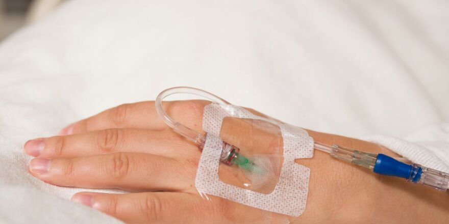 Close up hand of young patient with intravenous catheter for injection plug in hand during lying in the hospital bed.